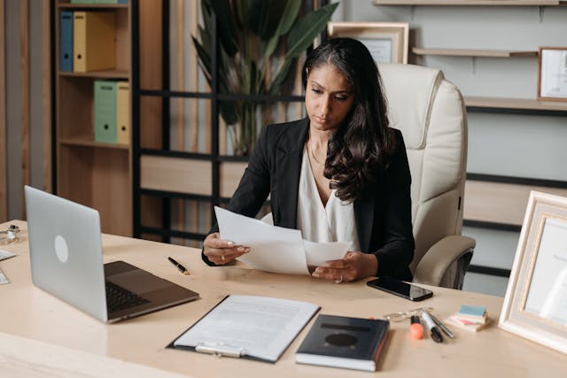 A professional woman sits at her desk in a business suit, focused on her work